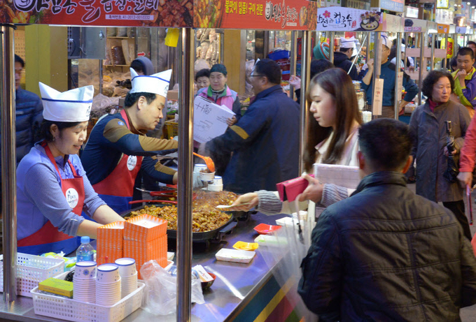 야시장 인기 매대인 '아짐손불곱창갈비'에서 관광객이 음식맛을 보고 있다.