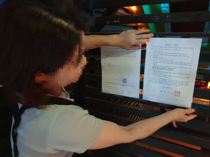 제주시청 대학로에서 노래주점을 운영하는 김모씨가 주점 입구에 붙어 있는 집합금지 조치서가 떨어지지 않도록 테이프를 손으로 누르고 있다.