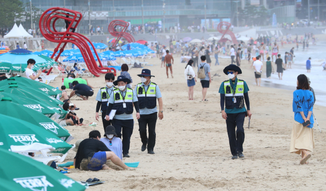 부산 지역 7개 해수욕장이 전면 개장한 이후 첫 주말인 4일 오후 부산 해운대해수욕장에서 단속요원들이 피서객들을 대상으로 마스크 착용 등 방역수칙 준수를 계도·단속하고 있다. 정대현 기자 jhyun@