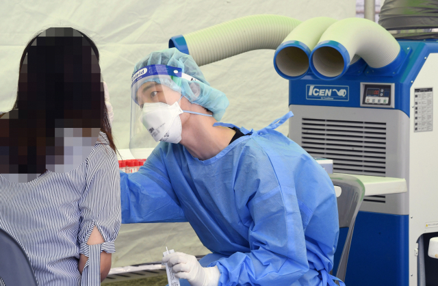 28일 창원스포츠파크 만남의 광장에 마련된 코로나19 임시선별진료소에서 한 의료진이 냉풍기 앞에서 내원객의 검체를 채취하고 있다./김승권 기자/